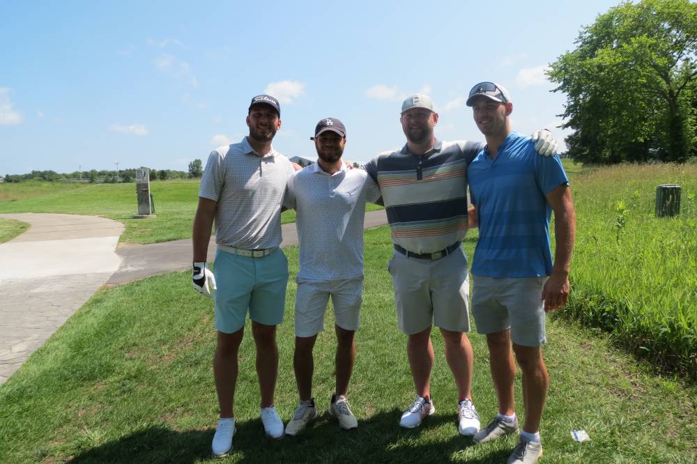 Four football alums posing for a photo together on the golf course.